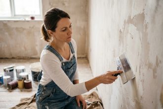Femme appliquant de l'enduit de rebouchage sur un mur en rénovation avant de peindre le salon