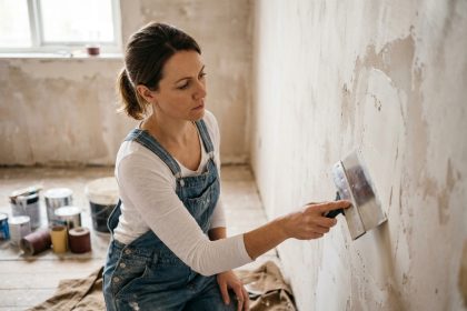 Femme appliquant de l'enduit de rebouchage sur un mur en rénovation avant de peindre le salon