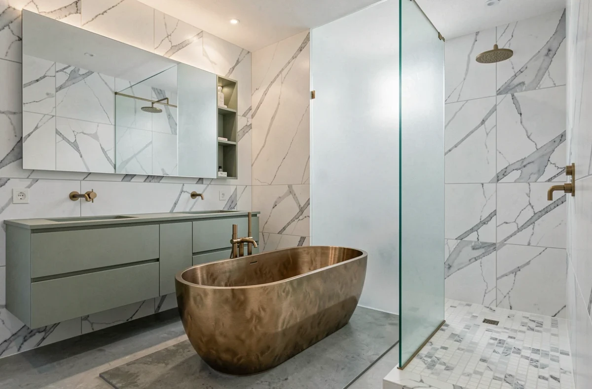 Salle de bain de luxe rénovée au Cannet avec baignoire ovale en laiton brossé, marbre Carrara et double vasque en laque sauge